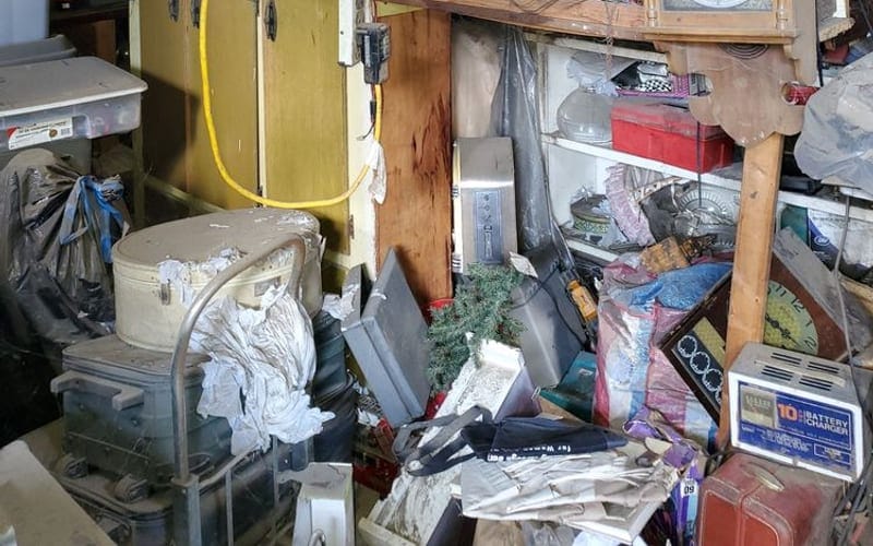 Old microwave, clocks and electrical clutter packed onto workshop shelving in Largo