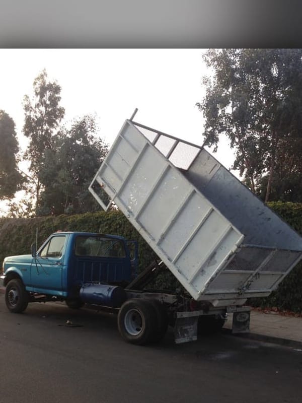 Hauling truck with its bed raised, tipping a full load at the county disposal complex