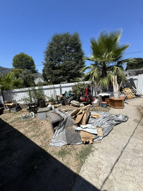 Fallen timber, tarp and storm debris spread across a fenced back yard in Largo, FL