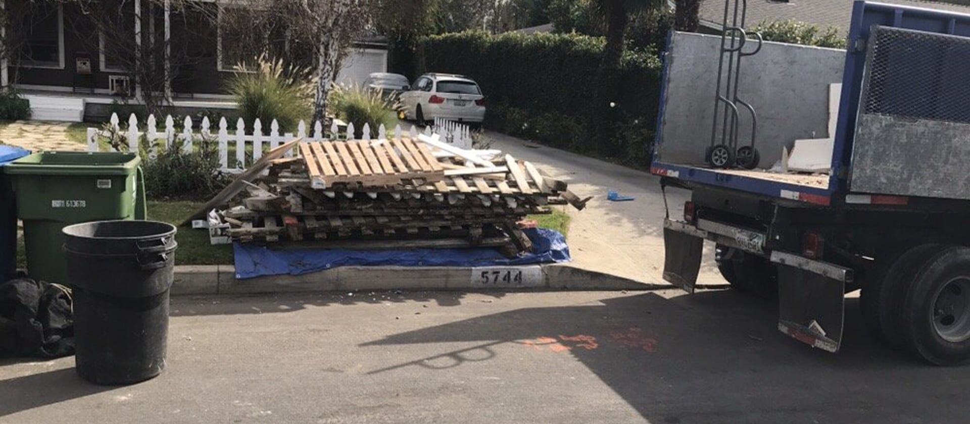 Stacked pallets and timber decking on a driveway beside a hauling truck and hand dolly