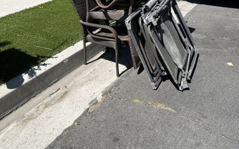Folding patio chairs and a wicker chair stacked at the curb in Largo, FL