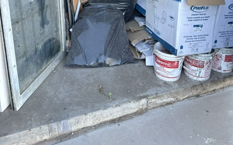 Bagged waste, paint buckets, old window panes and boxes stacked against a wall during a cleanout
