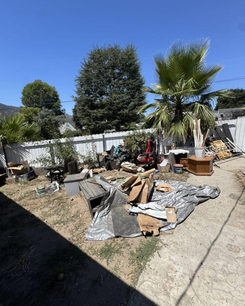 Timber, tarp and yard debris spread across a back yard for removal in Largo, FL